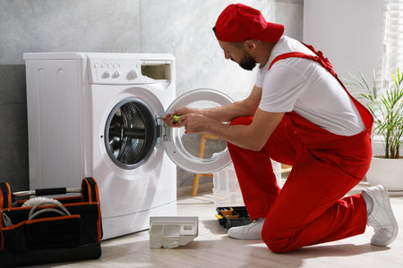 Professional repairman fixing broken washing machine indoorsの写真素材
