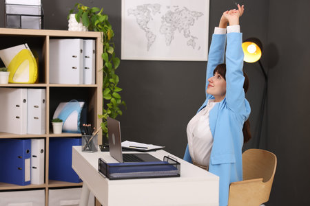 Young businesswoman stretching her arms and back at table in office