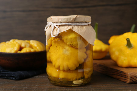 Pickled pattypan squashes in glass jar on wooden table, closeupの写真素材