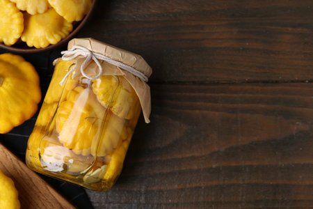 Pickled pattypan squashes in jar, bowl and fresh ones on wooden table, flat lay. Space for textの写真素材