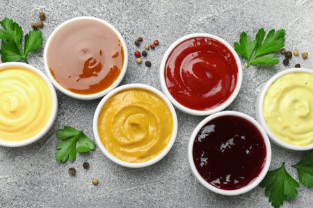 Different tasty sauces in bowls, parsley and peppercorns on gray table, flat layの写真素材