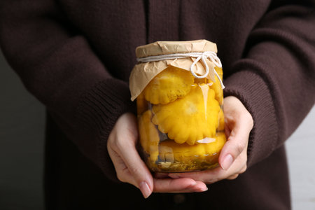 Woman with glass jar of pickled pattypan squashes against light gray background, closeupの写真素材