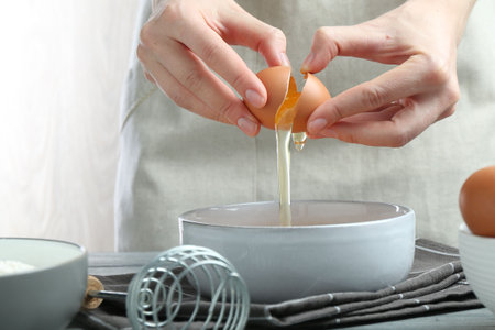 Woman breaking egg at table indoors, closeup