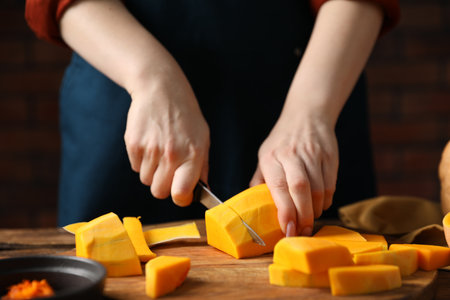 Woman peeling pumpkin at table against brick wall, closeupの写真素材