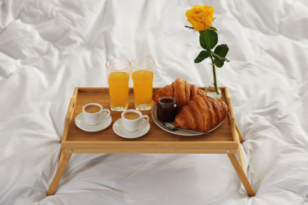 Tray with delicious breakfast and rose on bed in hotel room, closeupの写真素材