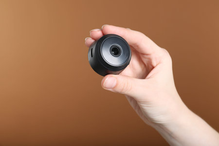 Woman with hidden camera on brown background, closeup. Space for text