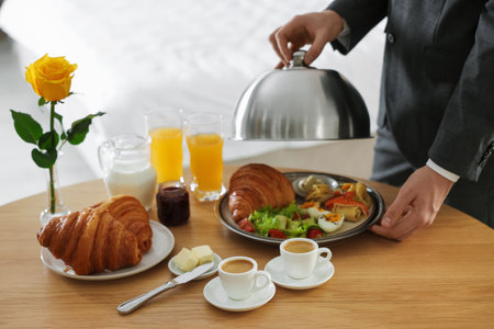 Waiter serving breakfast on wooden table in hotel room, closeupの写真素材