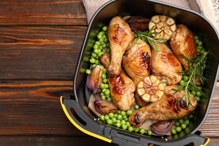 Air fryer basket with grilled chicken drumsticks, spices and green peas on wooden table, top view. Space for textの写真素材