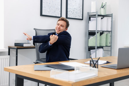 Young businessman stretching his arm at table in officeの写真素材