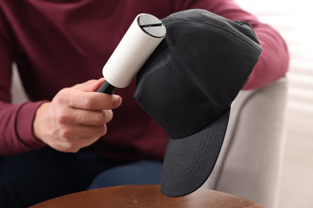 Man cleaning baseball cap with lint roller at home, closeup