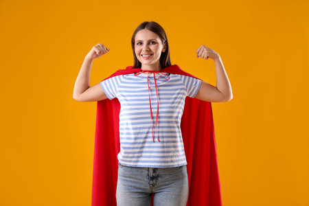 Woman wearing superhero cape on yellow backgroundの写真素材