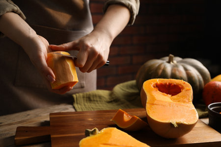 Woman peeling pumpkin at wooden table, closeup