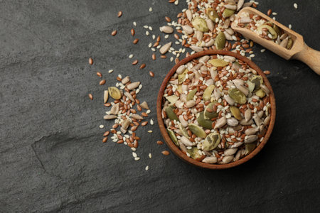 Mix of seeds in bowl and scoop on black textured table, flat lay. Space for textの写真素材
