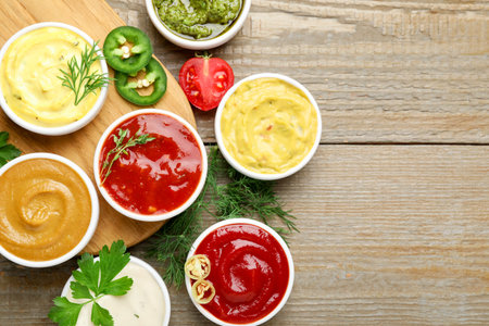 Different sauces and herbs on wooden table, flat lay. Space for text