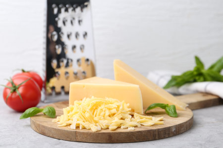 Grater, tomatoes, basil, grated and pieces of cheese on light table, closeup. Space for text