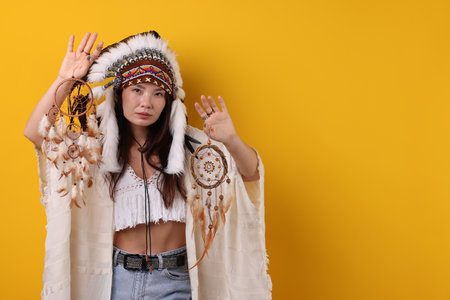 Shaman woman in native American Indian headdress with dreamcatchers on orange backgroundの写真素材