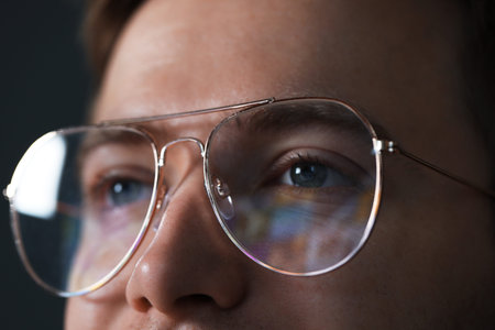 Man wearing glasses with reflection on dark background, closeup