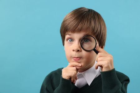 Little boy with magnifying glass on light blue background. Space for textの写真素材