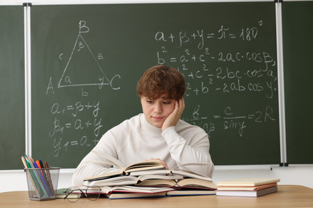Back to school. Student studying at wooden desk against chalkboard with math assignment indoorsの写真素材