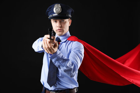 Police officer with gun wearing superhero cape on black background