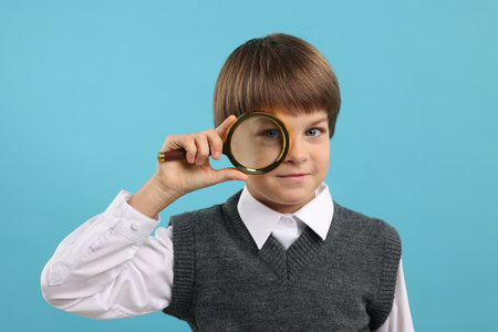 Little boy with magnifying glass on light blue backgroundの写真素材