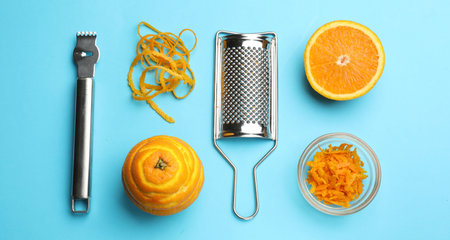 Orange zest, fresh fruits, grater and zester tool on light blue background, flat layの写真素材