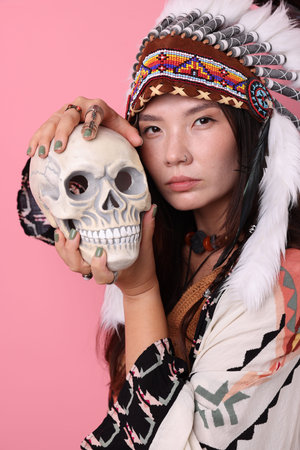 Shaman woman in native American Indian headdress with skull on pink background