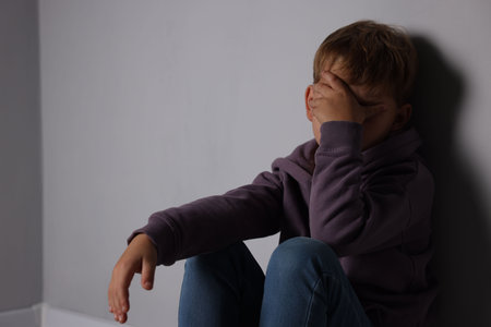 Upset little boy near light gray wall indoors, space for text