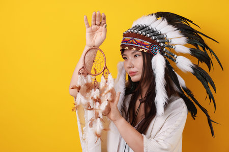 Shaman woman in native American Indian headdress with dreamcatcher on orange background, space for...