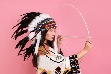 Shaman woman in native American Indian headdress with bow on pink background