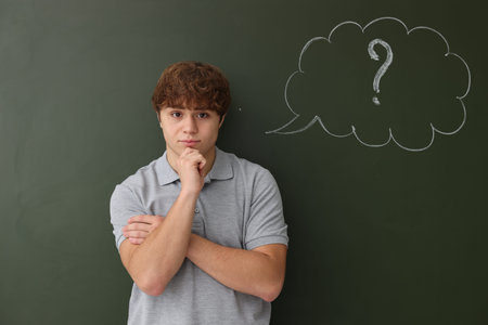 Back to school. Thoughtful boy near chalkboard with drawn thought bubble and question mark indoors