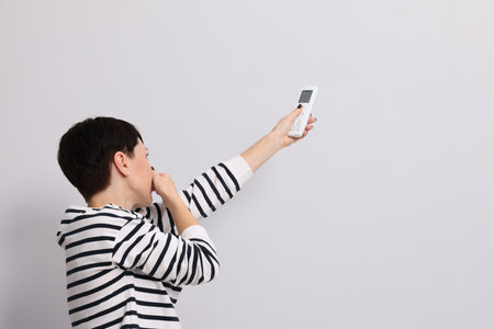 Woman with remote control feeling smell from air conditioner near light wall indoors, space for textの写真素材