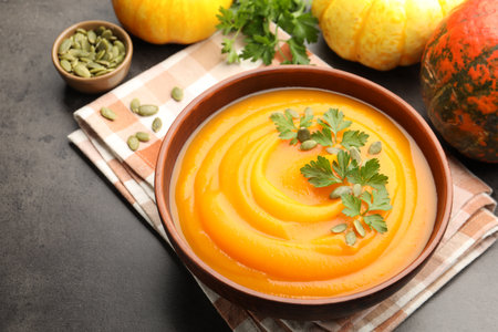 Tasty pumpkin cream soup with parsley and seeds in bowl on gray textured table, closeupの写真素材