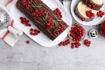 Delicious Yule log (traditional Christmas cake) with redcurrant and decor on gray textured table, flat lay. Space for textの写真素材