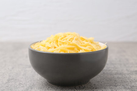 Grated cheese in bowl on gray table, closeup