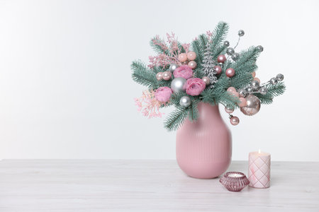 Winter composition with fir tree branches, flowers, Christmas decor in vase and burning candles on wooden table against white background. Space for textの写真素材