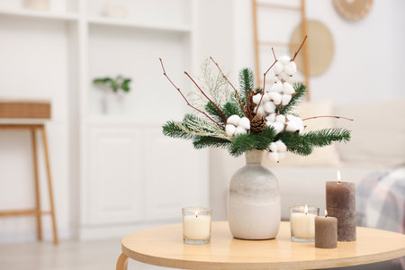 Winter composition with fir tree branches, cotton flowers in vase and burning candles on wooden table indoors, closeup. Space for textの写真素材