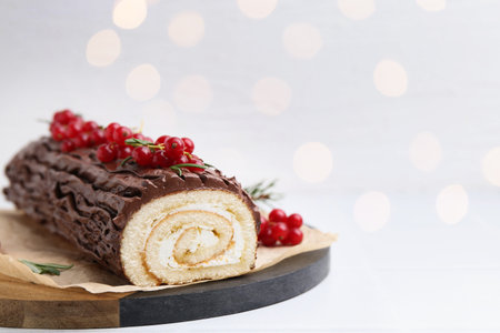 Delicious Yule log (traditional Christmas cake) with redcurrant on table against blurred lights, closeup and space for text. Bokeh effectの写真素材