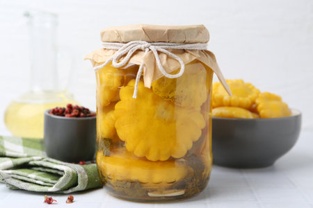 Pickled pattypan squashes in glass jar on white tiled table, closeupの写真素材