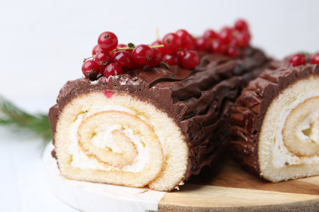 Delicious Yule log (traditional Christmas cake) with redcurrant on white table, closeupの写真素材