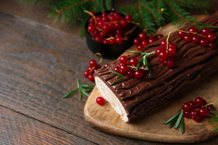 Delicious Yule log (traditional Christmas cake) with redcurrant and fir tree branches on wooden table, closeup. Space for textの写真素材