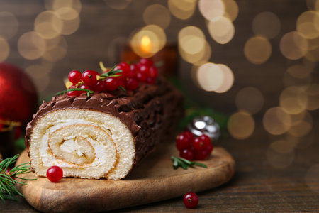 Delicious Yule log (traditional Christmas cake) with redcurrant on wooden table, closeup. Space for textの写真素材