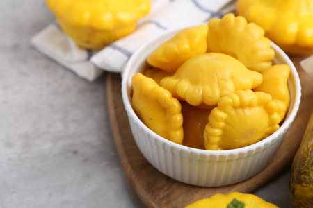 Pickled pattypan squashes in bowl on light gray table, closeup. Space for text