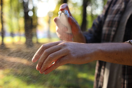 Man spraying tick repellent onto arm in park, closeup. Space for textの写真素材