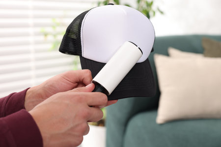 Man cleaning baseball cap with lint roller at home, closeup