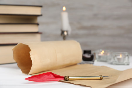 Scroll of old parchment paper, fountain pen, inkwell, books and burning candles on white wooden table, closeupの写真素材