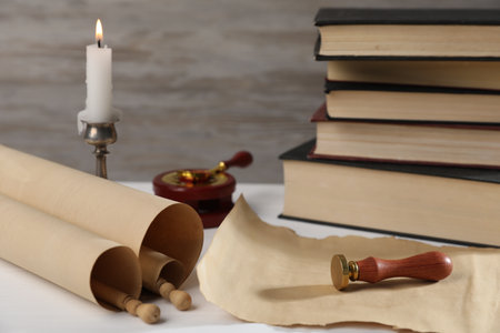 Scroll of old parchment paper, wax stamp, sealing spoon, books and burning candle on white wooden table, closeupの写真素材