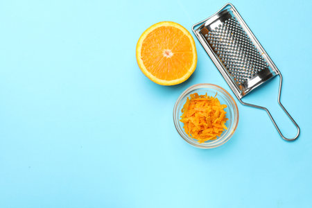 Orange zest, fresh fruit and grater on light blue background, flat lay. Space for textの写真素材