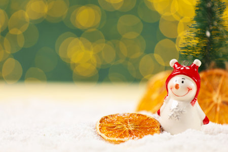 Cute decorative snowman and dried orange slices on artificial snow against blurred lights, closeupの写真素材