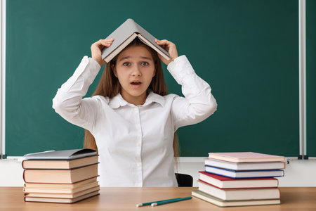 Back to school. Student with books at wooden desk against chalkboard indoorsの写真素材